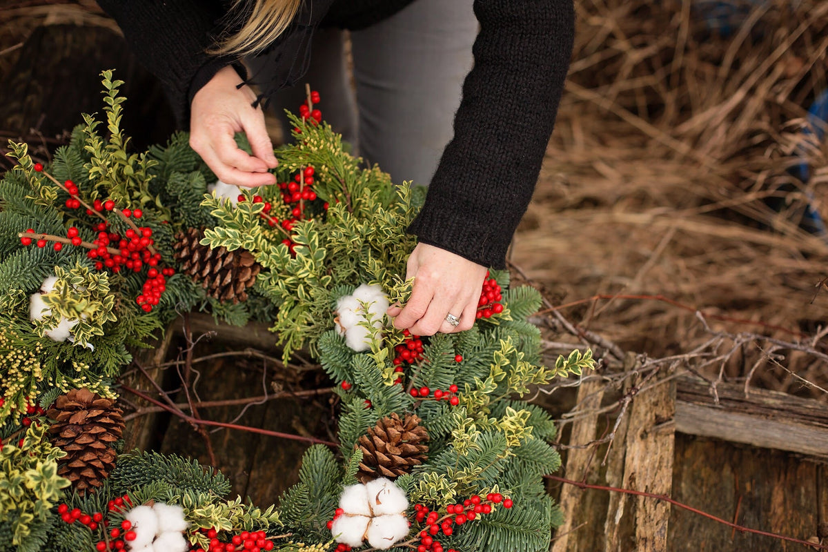Someone putting the finishing touches on a winter wreath with greens, red berries and pinecones.
