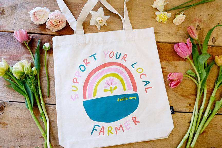 Off-white canvas bag with a rainbow logo saying support your local farmer in pink, teal, yellow and coral letters.