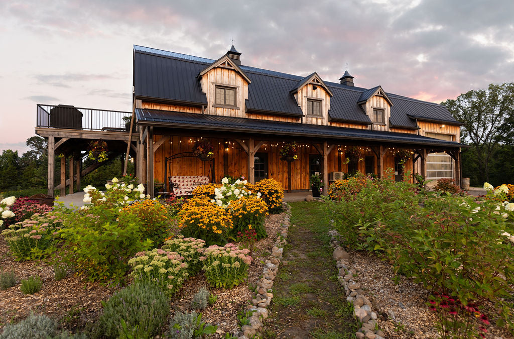 Straight on shot of wooden barn with black metal roof, a path through perennial gardens leads to the barn.