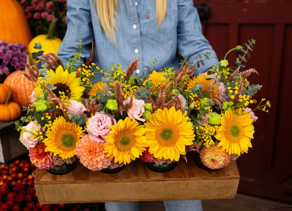 A wooden tray holding eight mason jar arrangements in festive colours.