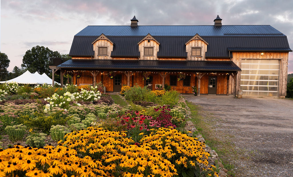 Wooden barn with a white event tent behind it and the parking lot in the front right.