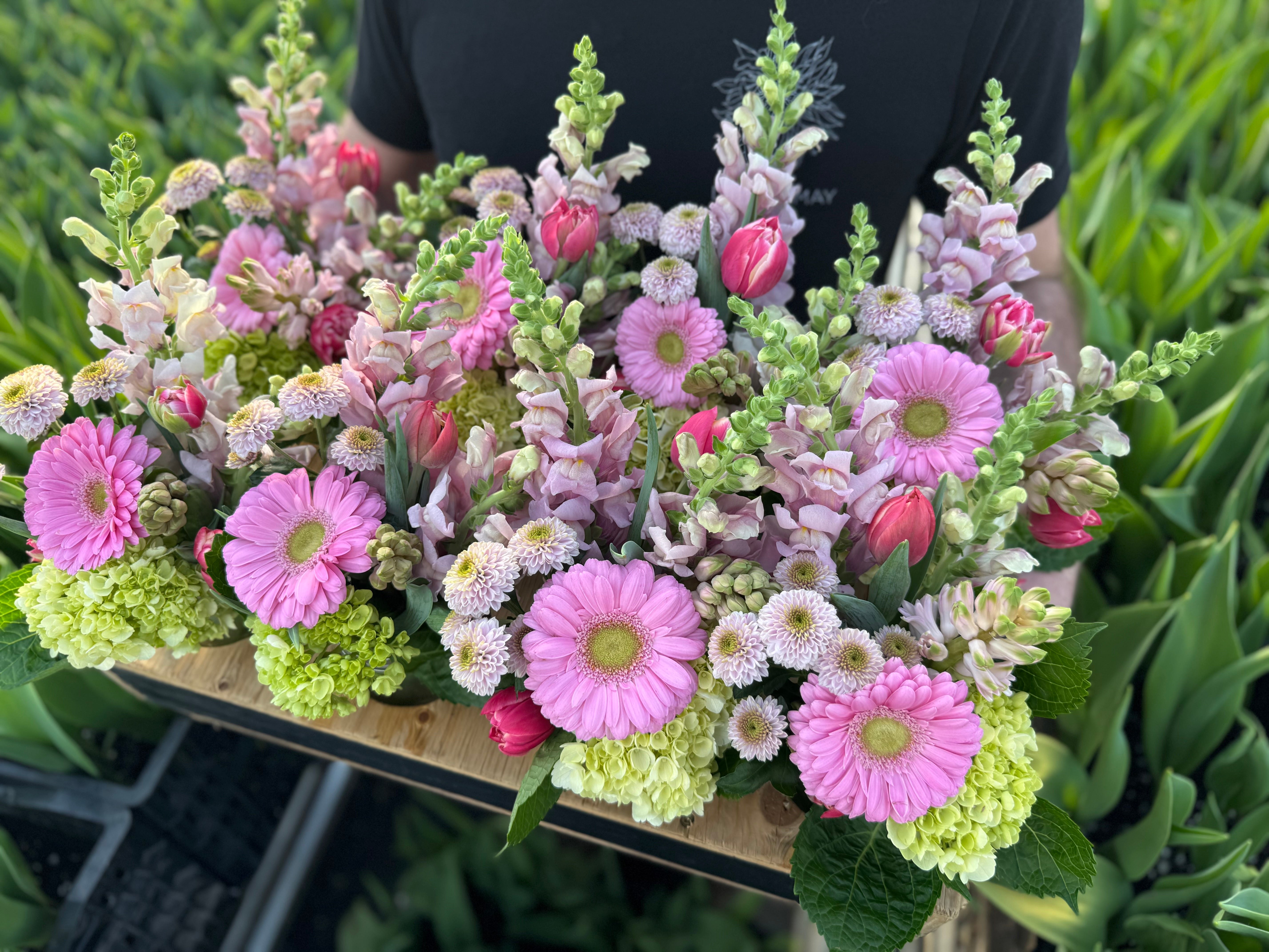 A mason jar arrangement of various flowers including pink gerbera daisies, snapdragons, and other mixed flowers.