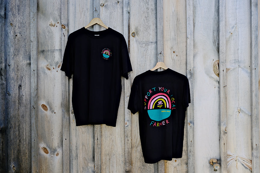 Two black T-shirts with graphic prints, one featuring a multicolored design with text 'DAHLIA MAY FARMER' and the other a simple, solid black design with a rainbow graphic on the front.