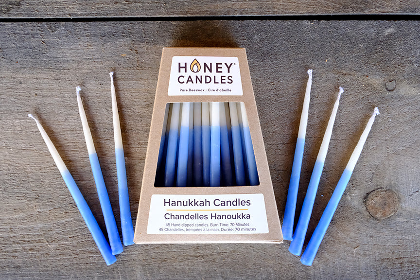 A set of blue and white beeswax Hanukkah candles displayed in front of a kraft box packaging.
