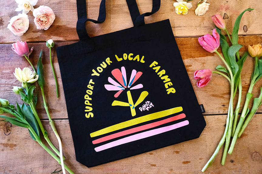 Black canvas bag with a flower logo and "support your local farmer" in yellow letters above the flower