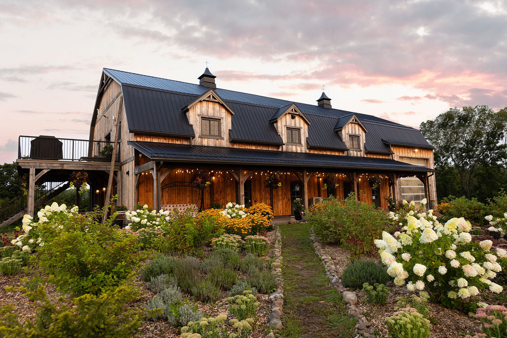 A wooden barn with black metal roof sits behind a perennial garden.