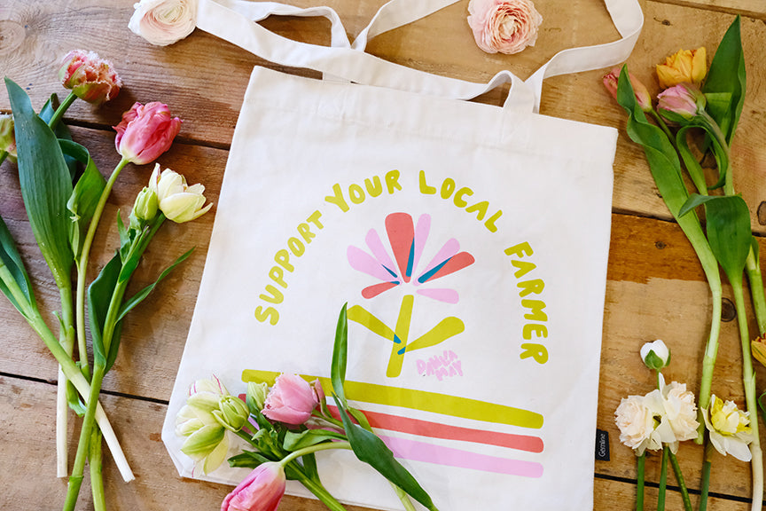 Off-white canvas bag with flower logo and 'support your local farmer' in yellow letters above the flower.