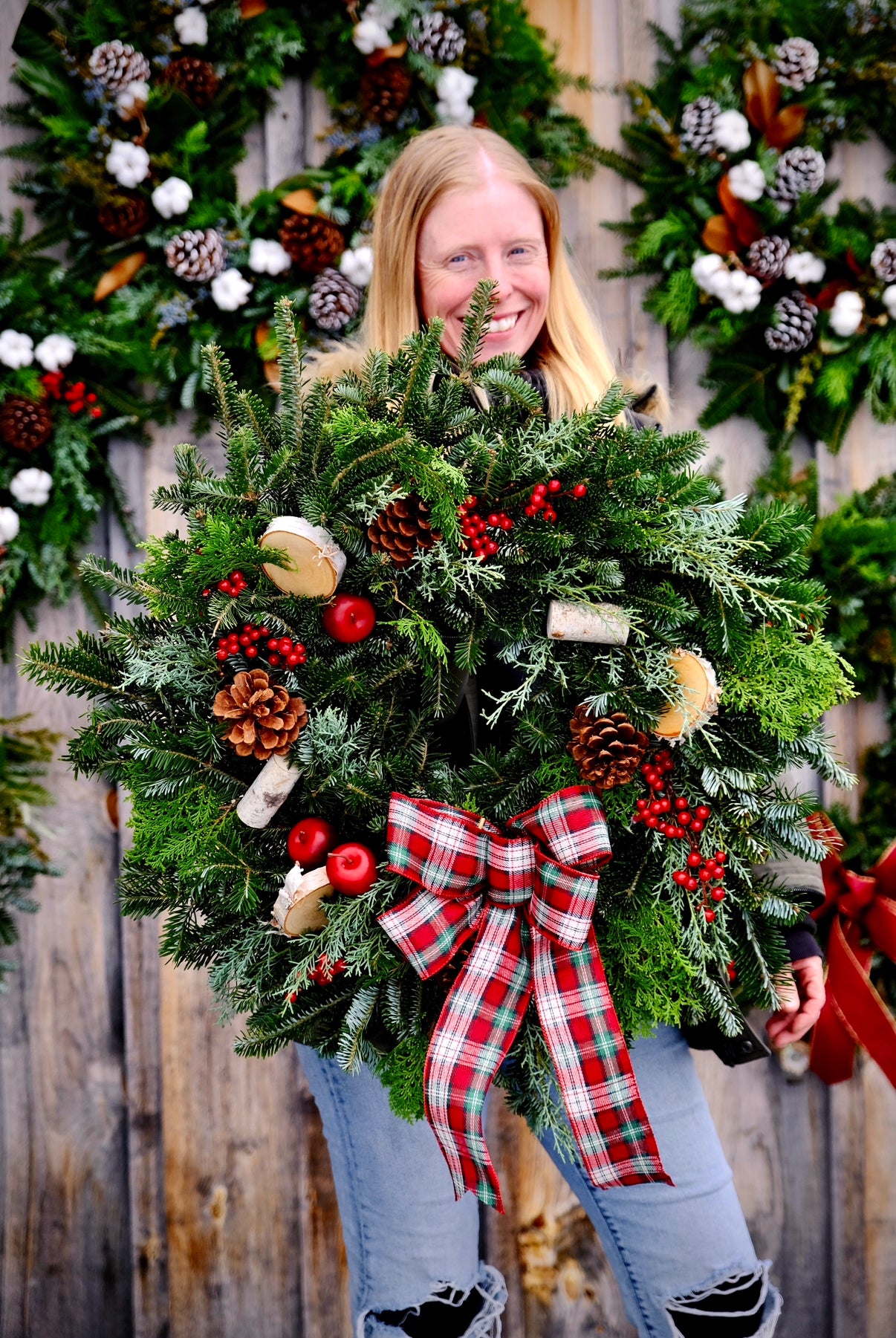 Person holding a large Christmas wreath with a plaid bow against a wooden background