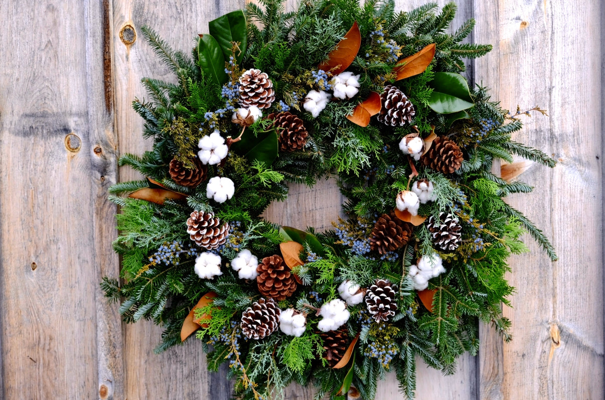 Christmas wreath with pine cones, white flowers, and greenery on a wooden door.