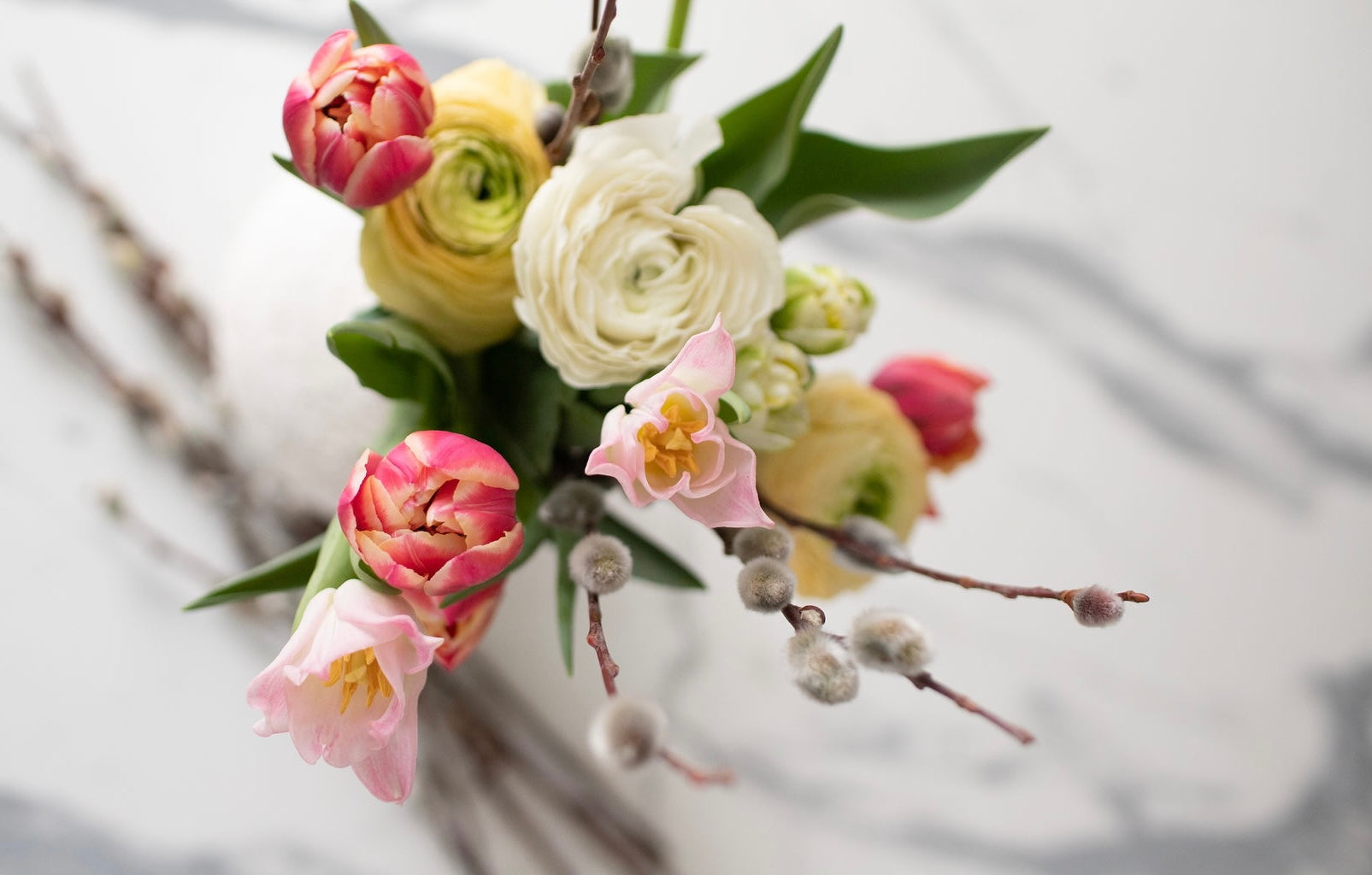 A subscription bouquet shown from above with tulips, ranunculus, tulips, and pussy willow stems.