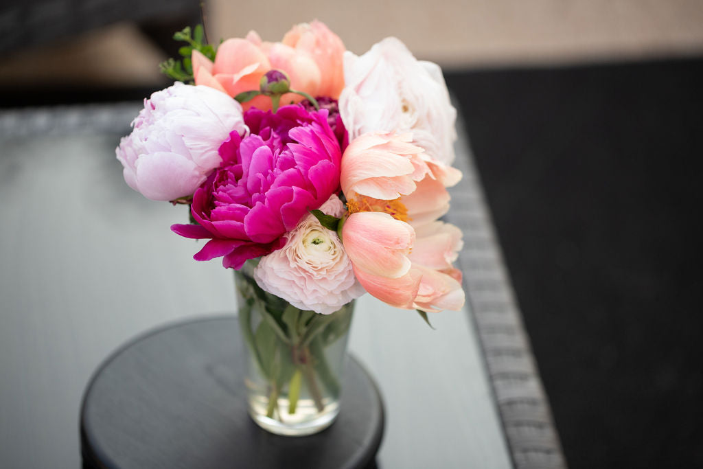 A bouquet of peonies and ranunculus in a glass vase.