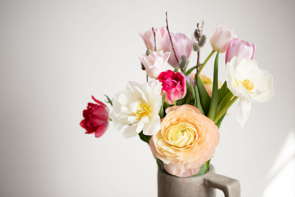 A bouquet of ranunculus and tulips in peach, dark pink, white and light purple.