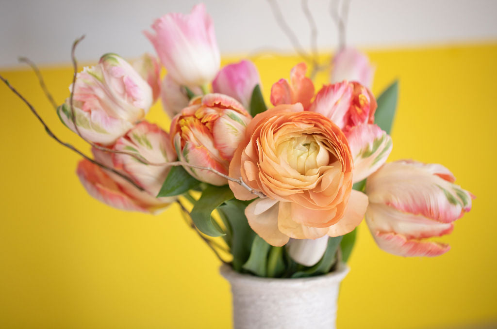 Close-up of a bouquet featuring peach ranunculus, light pink and white tulips and curly willow.