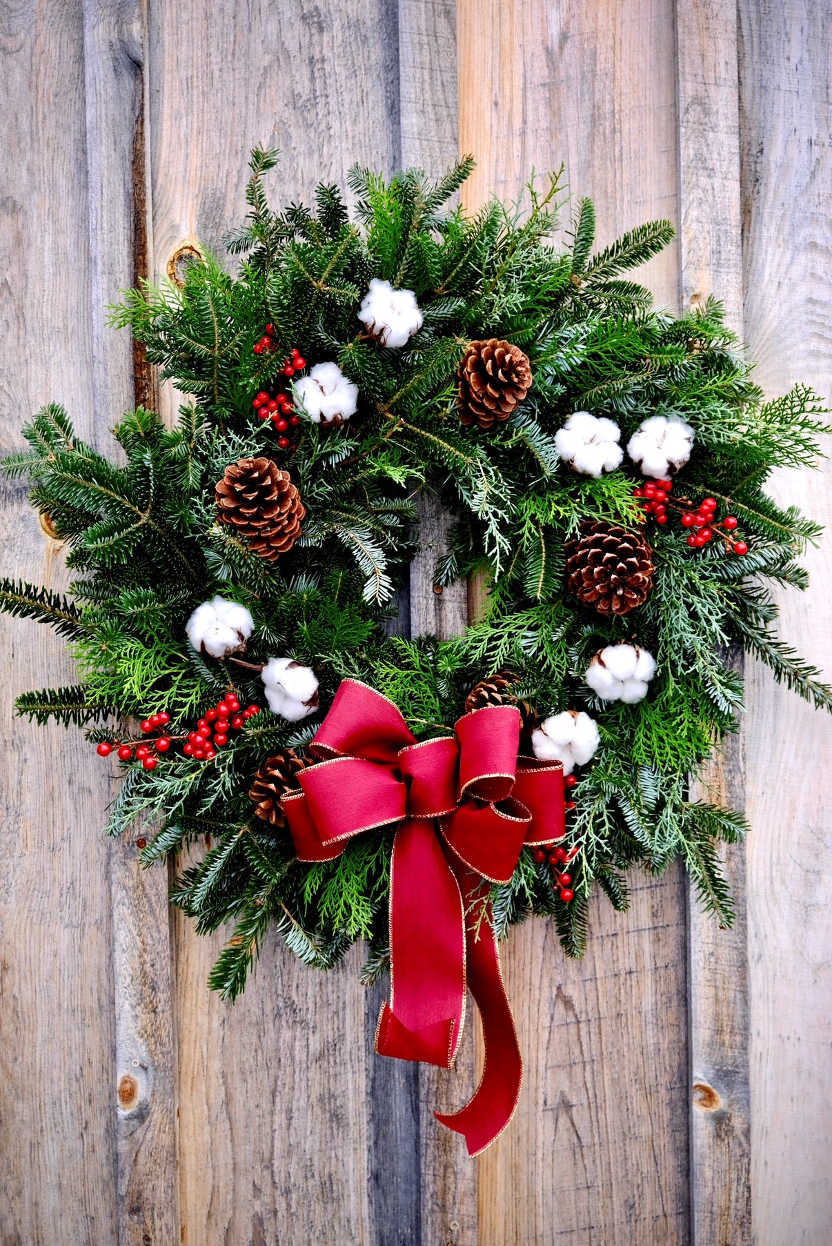 Christmas wreath with greenery, pinecones, berries, and a red bow on a wooden background