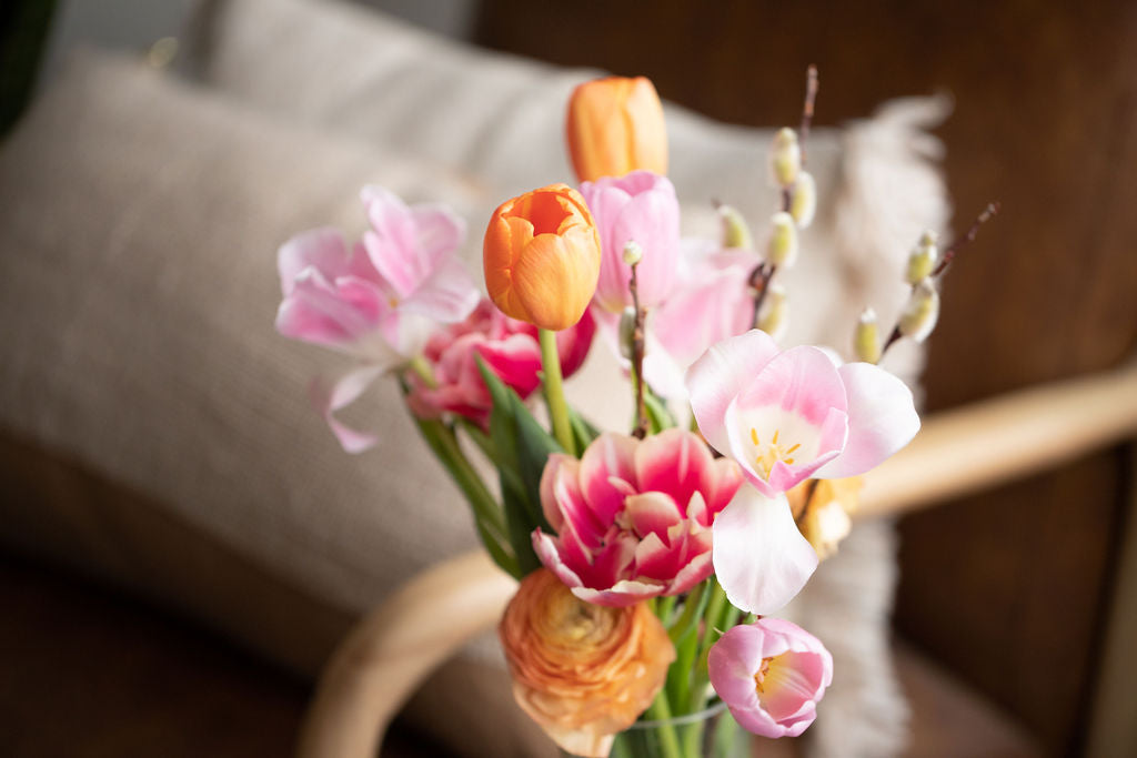 Close up of a bouquet featuring light orange, pink and white tulips and ranunculus. 